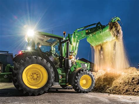 Thematic photo of John Deere R-series front loader working at dusk or night with lights on