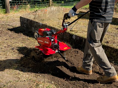 The Honda FJ 500 DER2 cultivator at work in a garden, showing its adjustable handlebars and working width.