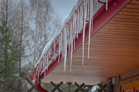 Zaspy śniegu i sople lodu na dachu budynku
