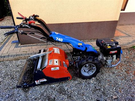 Ilustracja przedstawiająca ciągnik jednoosiowy z zamontowaną glebogryzarką w akcji na polu.