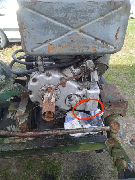 Zdjęcie przedstawiające uszkodzony traktor z widocznym wyciekiem oleju pod drzewem czereśniowym.