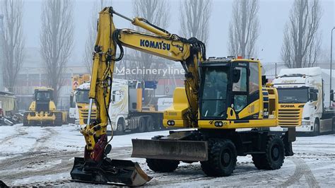 Komatsu PW118 na budowie, pracująca w warunkach miejskich, z widocznym szybkozłączem