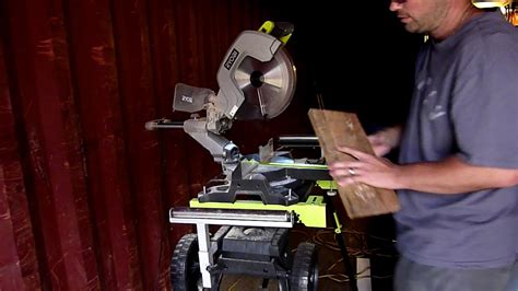 The Ryobi EMS305RG miter saw in action, cutting a wooden board with an LED light illuminating the work area.