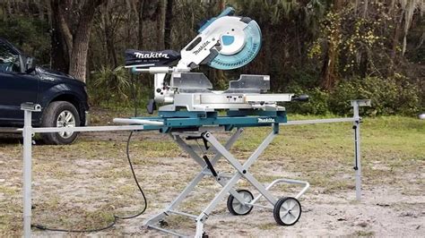Makita LS1219L z wysuniętymi podwójnymi prowadnicami przesuwnymi, na tle drewnianych belek.
