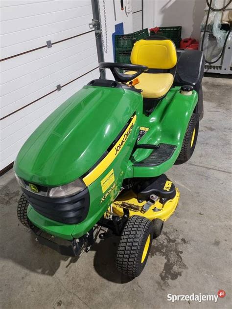 Schemat budowy traktorka John Deere X300R z zaznaczonymi elementami konstrukcyjnymi, takimi jak rama, oś przednia i fotel operatora.