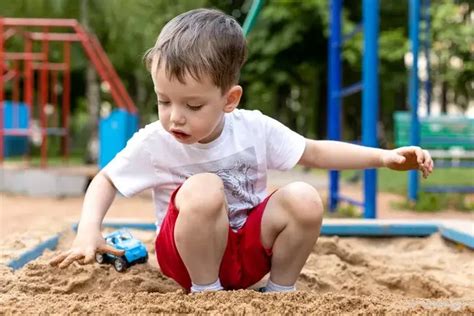 Dziecko bawiące się pojazdami budowlanymi w piaskownicy, pokazujące ruchome elementy zabawek