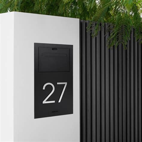 Thematic photo of a modern letterbox integrated into a wall, with a visible camera lens and backlit house number