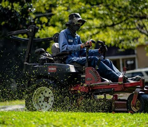 Zdjęcie przedstawiające operatora pracującego kosiarką zero-turn w dużym, złożonym ogrodzie